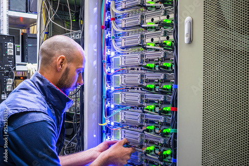  A man works with telecommunications. The technician switches the Internet cable of the powerful routers. A specialist connects the wires in the server room of the data center.