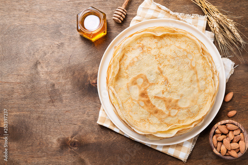 Crepes, thin pancakes with honey and nuts on a white plate . Wooden background .