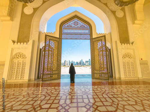 Woman with abaya dress looks at views of skyscrapers of Doha West Bay skyline outdoors State Grand Mosque in Doha, Qatar, Middle East, Arabian Peninsula.