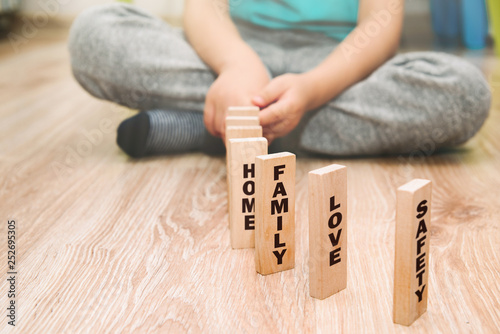 The most important family values presented by the child. The little boy arranges wooden blocks with the words HOME, LOVE, FAMILY. The boy shows what he needs to be a happy child.