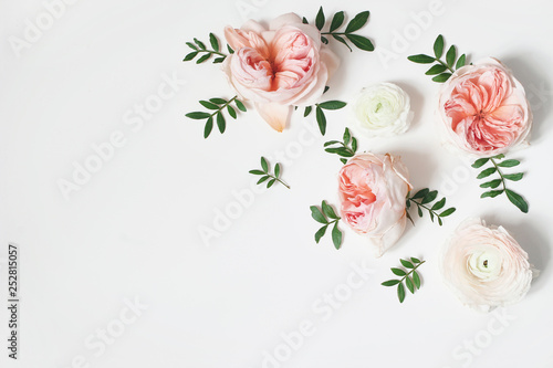Decorative corner, floral composition with pink English roses, ranunculus and green leaves on white table background. Flower pattern. Flat lay, top view. Wedding or birthday styled stock photo.