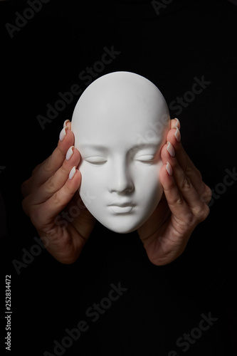Female hands close ears of plaster mask face on a black background. Hear no evil. Concept three wise monkeys.