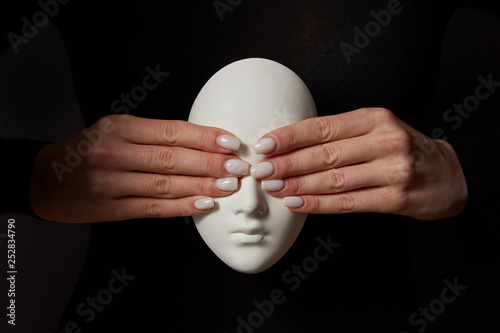Woman's fingers close eyes of gypsum mask face on a black background. See no evil. Concept three wise monkeys.