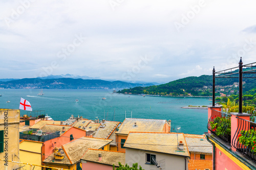 Top aerial view of Gulf of Spezia turquoise water, roofs of buildings in Portovenere, Palmaria island green hills, blue cloudy dramatic sky, Ligurian sea, Riviera di Levante, La Spezia, Liguria, Italy