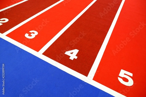 Diagonal view of colorful atheltic running track for children with white numbers 2,3,4,5 in indoor stadium