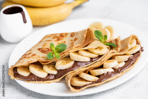 Crepes stuffed with chocolate spread and banana on white plate. Thin pancakes, blini. Sweet dessert.