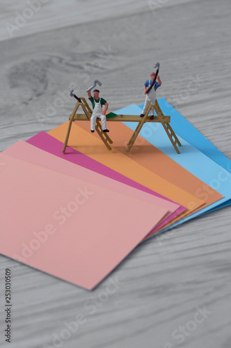 Colour paint swatch cards with miniature scale model painters and decorators on a grey wood background with pinks oranges and blues