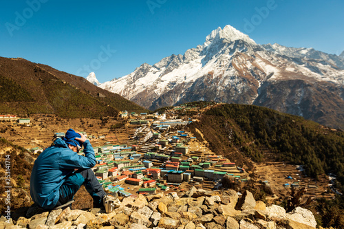 Everest trekking. A man sits on a hill with his head bowed and his arms around him. Altitude sickness. Near the mug. The man in focus. The background is blurred. Namche Bazaar. Nepal