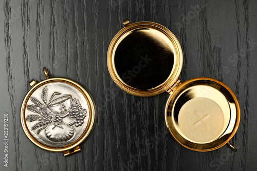 Host wafer of bread to be consecrated as the Body of Christ at Mass in a gold Pyx on a black oak table