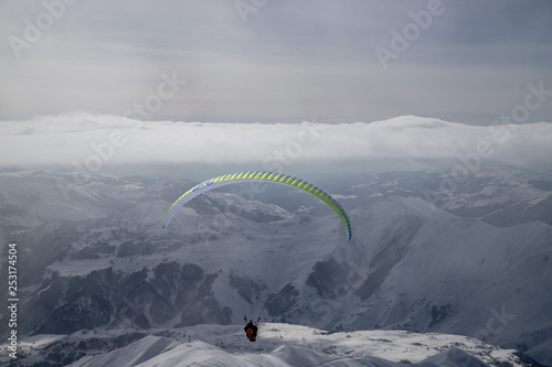 Paralotniarstwo w zaśnieżonych górach nad ośrodkiem narciarskim w słoneczny zimowy dzień. Góry Kaukazu. Gruzja, region Gudauri.