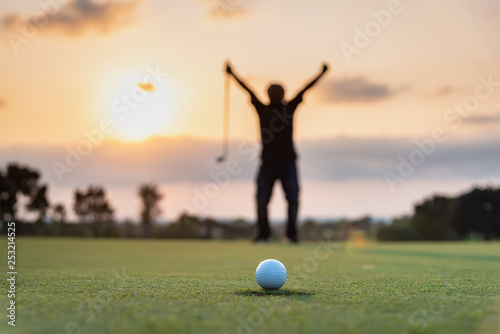 Silhouette golfer showing happiness when win in game , white golf ball on green grass of golf course with blur background.