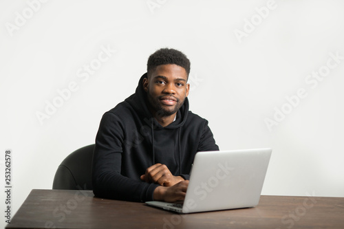 handsome african man in a tracksuit sits at a table with a laptop