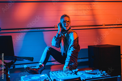 cheerful dj girl in glasses touching dj mixer in nightclub