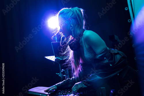 blonde stylish dj girl touching dj equipment in nightclub