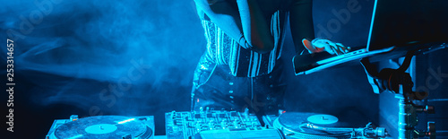 panoramic shot of dj woman using laptop in nightclub with smoke