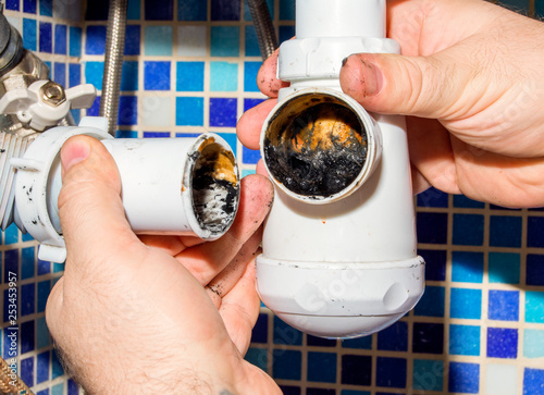 The plumber disassembles the siphon under the sink to clean it from dirt. House master.