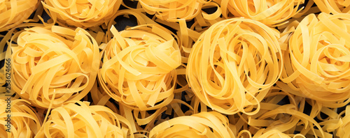 Uncooked fettuccine nest pasta texture background, banner