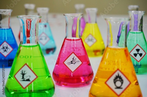 Many of Erlenmeyer flask with colorful solution and Variety type of chemical hazard warning symbols labels. Focus on Explosive sign,symbol.