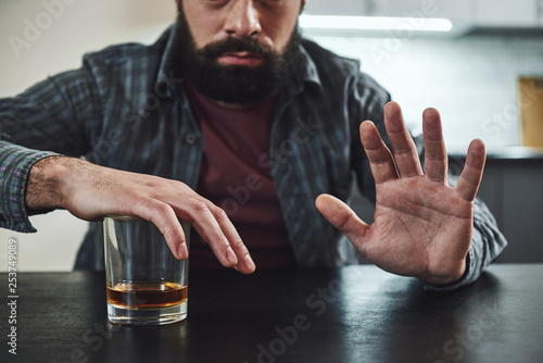 Forget past mistakes. Forget failures. Forget about everything except what you’re going to do now – and do it. Addicted man refuses to drink a glass of whiskey. Cropped image. Selective focus