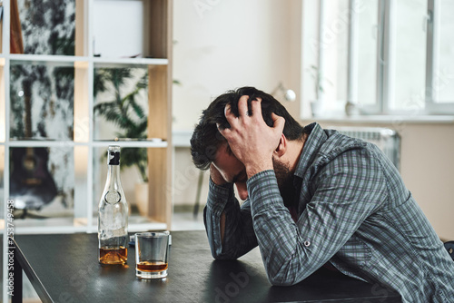 The most common way people give up their power is by thinking they don’t have any. Drunk man with glass and bottle of whiskey sitting at table in kitchen. Drinking alone. Male alcoholism concept