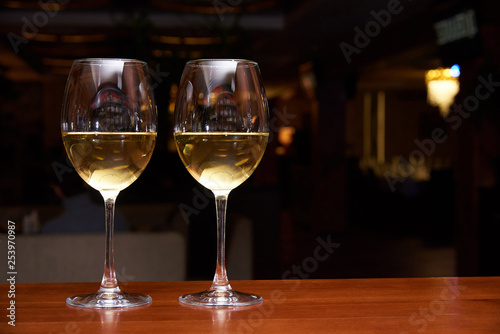 Two glasses of white wine with a reflection on the bar.