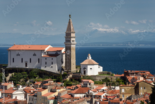 Piran Slovenia with St George's Cathedral belfry and baptistery on the Gulf of Trieste with snow capped Kanin mountains and distant Monfalcone Italy