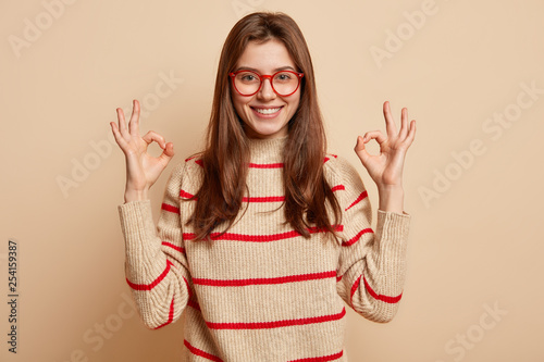 Cheerful Caucasian lady shows zero gesture with both hands, being optimistic, expresses approval, smiles gently at camera. Satisfied customer gives recommendation, suggests to buy nice product