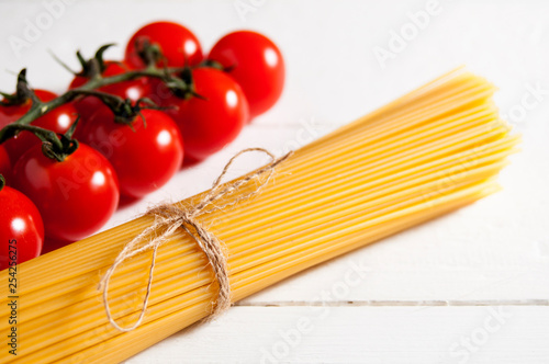 Bunch of spaghetti and cherry tomatoes on a white wooden background.