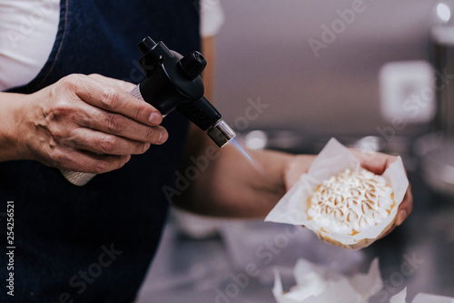 Tartlet with a meringue and kitchen torch blowtorch with blue flame. woman hand holdings blowtorch. bakery concept