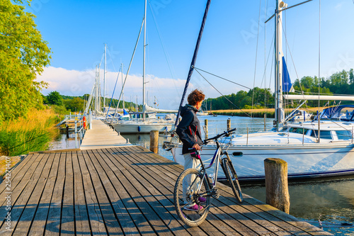SEEDORF PORT, RUGEN ISLAND - MAY 27, 2018: Woman with bicycle standing in beautiful marina on coast of Rugen island, Baltic Sea, Germany. It is very popular cycling destination in summer season.