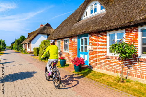 Young woman riding bike in Moritzdorf village with typical red brick house with straw roof along road, Baltic Sea, Germany