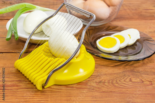 Whole and sliced eggs and egg slicer on rustic table