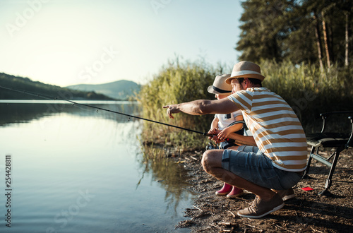 A mature father with a small toddler son outdoors fishing by a lake.