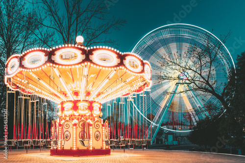 Illuminated Attraction Ferris Wheel And Carousel Merry-go-round On Summer Evening In City Amusement Park.