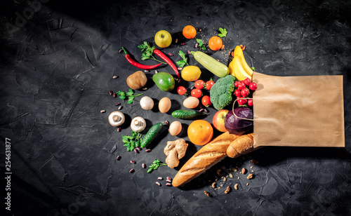 Healthy food in full paper bag of different products vegetables and fruits on dark background