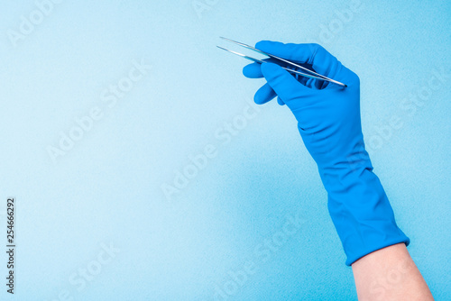 Hand in blue glove holding dental tweezers on light blue background