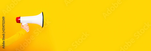megaphone in hand on a yellow background, panoramic image, attention concept announcement