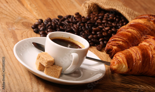 Coffee white cup, croissants on wooden table and roasted coffee beans. Breakfast concept