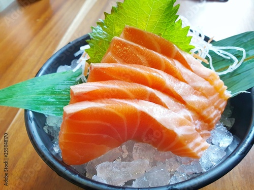 Japanese food style, Close up of salmon slice on bamboo leaves on ice in black bowl on wooden table, Salmon sashimi is Japanese traditional, Selective focus