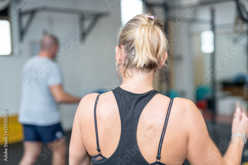 Back view of woman training at the gym with personal trainer on the background