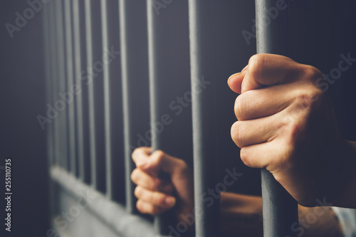 Man in prison hands of behind hold Steel cage jail bars. offender criminal locked in jail. filter dark vintage.