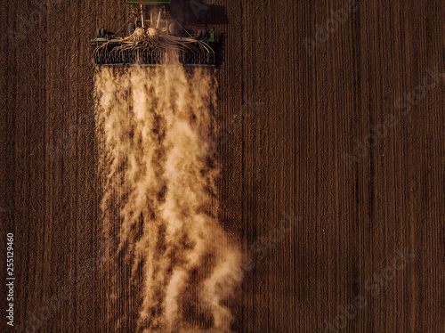 Tractor cultivating field, kicking up rocks and dust in early morning