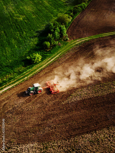 Tractor cultivating field, kicking up rocks and dust in early morning