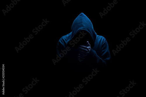 Man in black hood in the night darkness, dimly lit, concepts of danger, crime, terror