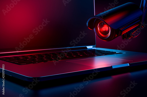 Computer observed by hostile looking camera as a metaphor of stalking or malicious software observing and tracking user. Copy space on laptop screen included. 3D rendering
