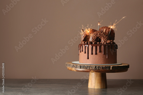 Sweet chocolate cake with sparklers on table against color background