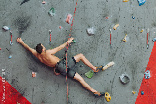 young shirtless man reaching to the rope during bouldering. full length photo