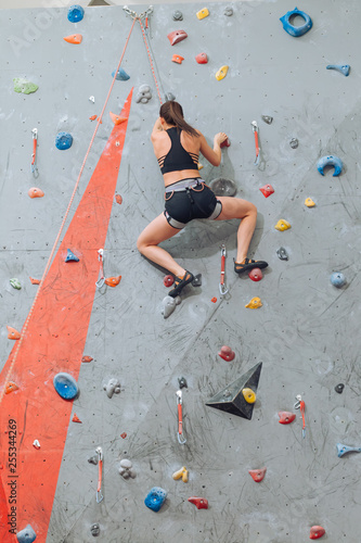 Young flexible woman climbing up on wall in gym, rear view full length photo. hobby, lifestyle, free time