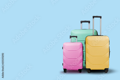 Three multi-colored plastic suitcases on wheels on a blue background. Travel concept, vacation trip, visit to relatives
