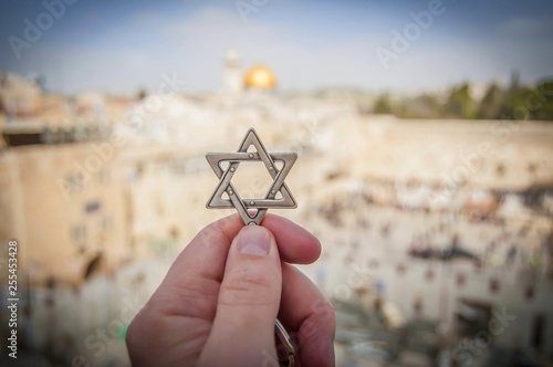 JERUSALEM, ISRAEL. February 15, 2019. Hand holding a Star of David, a Jewish religious symbol against the Western wall of the Jewish Temple in the Old city of Jerusalem. Judaism Zionism concept image.